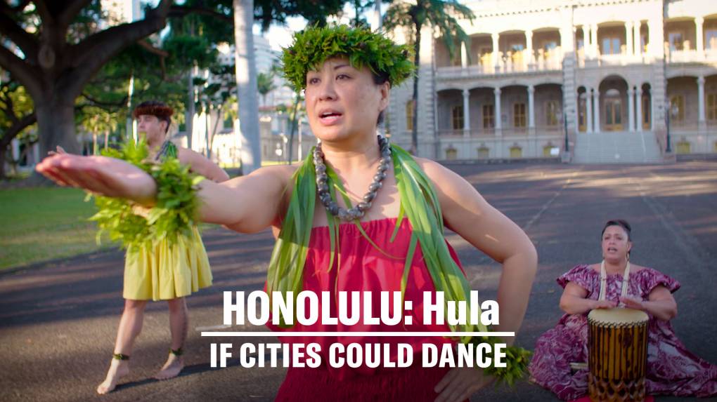 Female hula dancer in traditional attire extends her arm towards the camera.