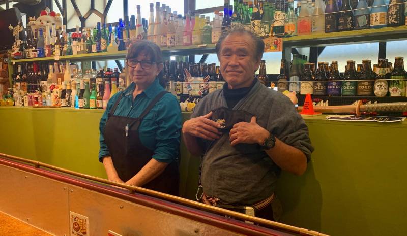 Owners Yolanda (left) and Mitsuhiro Nakamura stand behind the bar at their restaurant On the Bridge. 