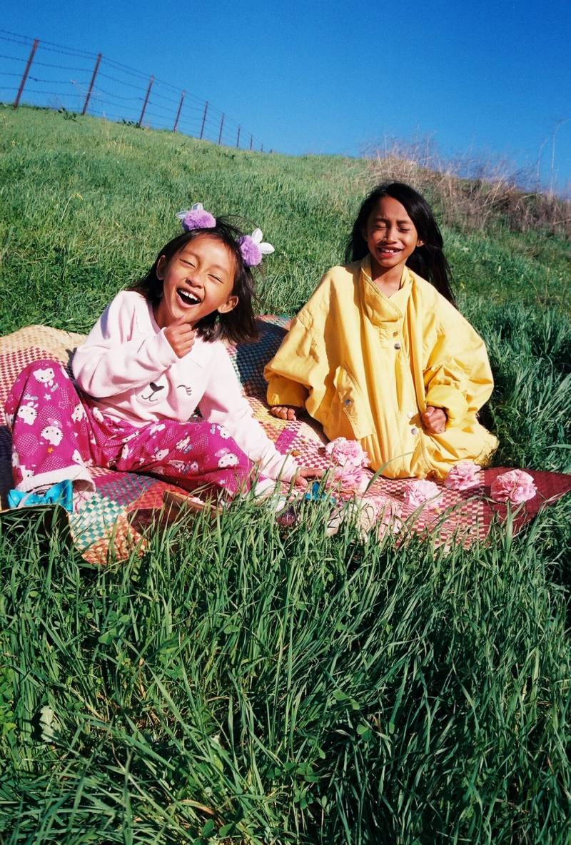 Been Milky's daughters smile and pose for a photo on a grassy hillside.
