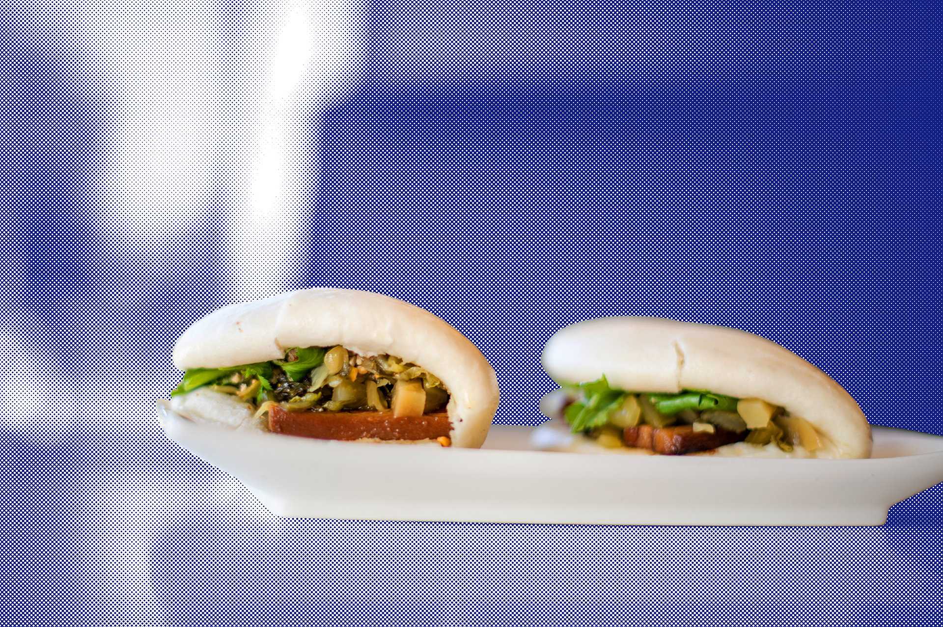 A pair of gua bao, or Taiwanese pork belly buns, on a white plate, against a stylized blue backdrop.