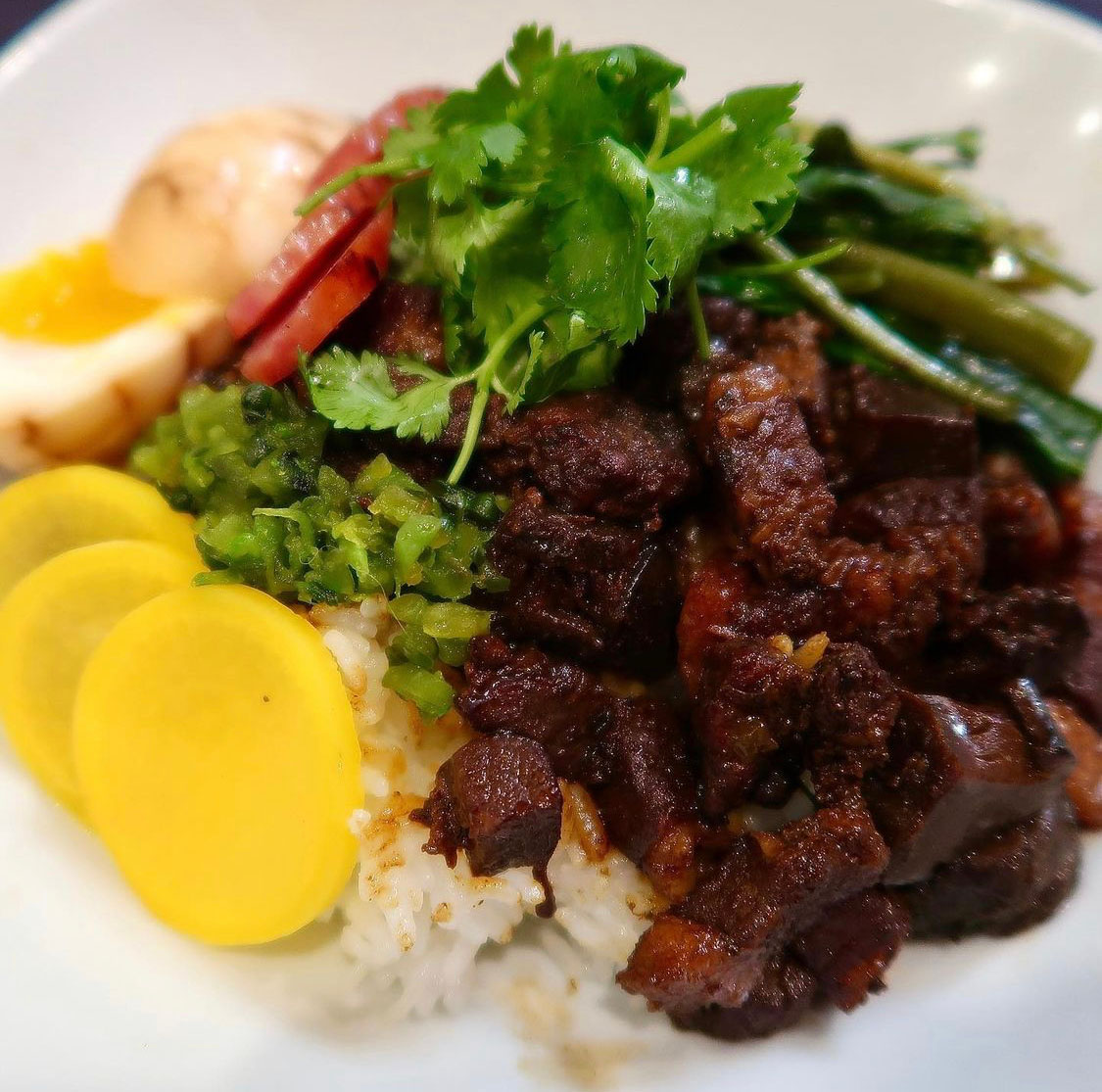 A bowl of lu rou fan, or braised pork rice, garnished with cilantro and yellow daikon pickles.