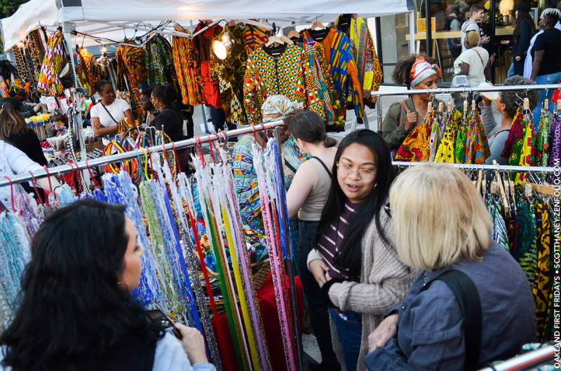 Women look at clothing in a festival booth filled with African fabrics.