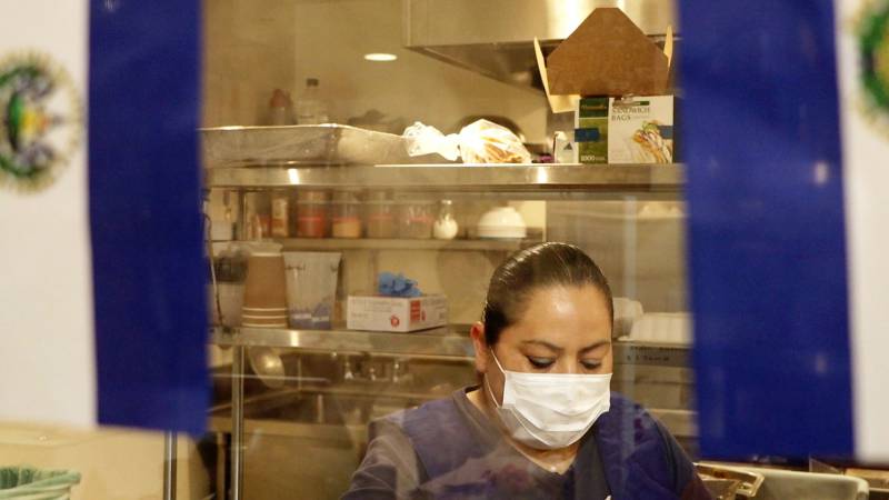 Estrella Gonzalez of Estrellita's Snacks prepares food in her commercial space at La Cocina kitchen while framed by the flag of El Salvador.