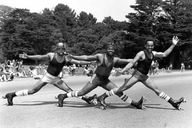 A black and white photo of The Golden Rollers. The three of them look like they are doing a Temptation-esque, in a diagonal formation striking a pose almost down in the splits -- really low to the ground --- with arms stretched out