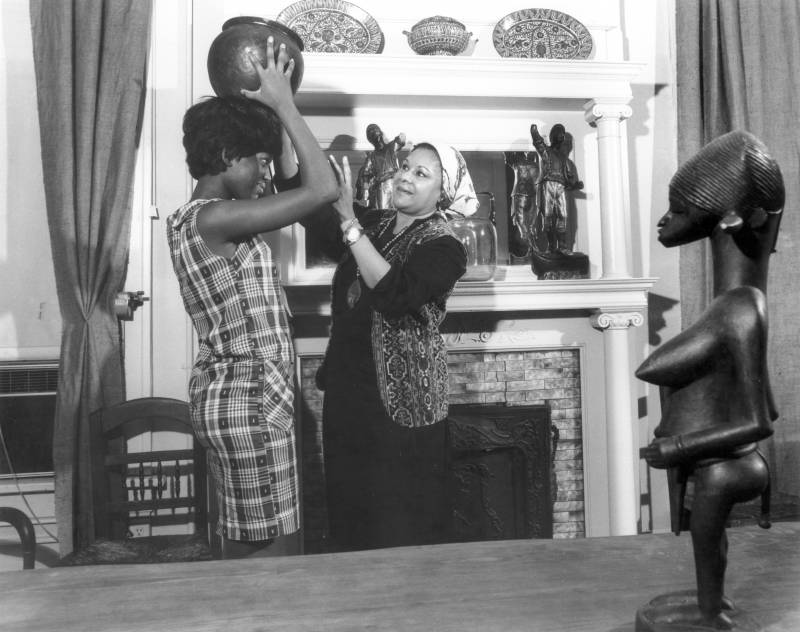 Katherine Dunham interacts with a visitor, who places a pot on her head, in her museum.