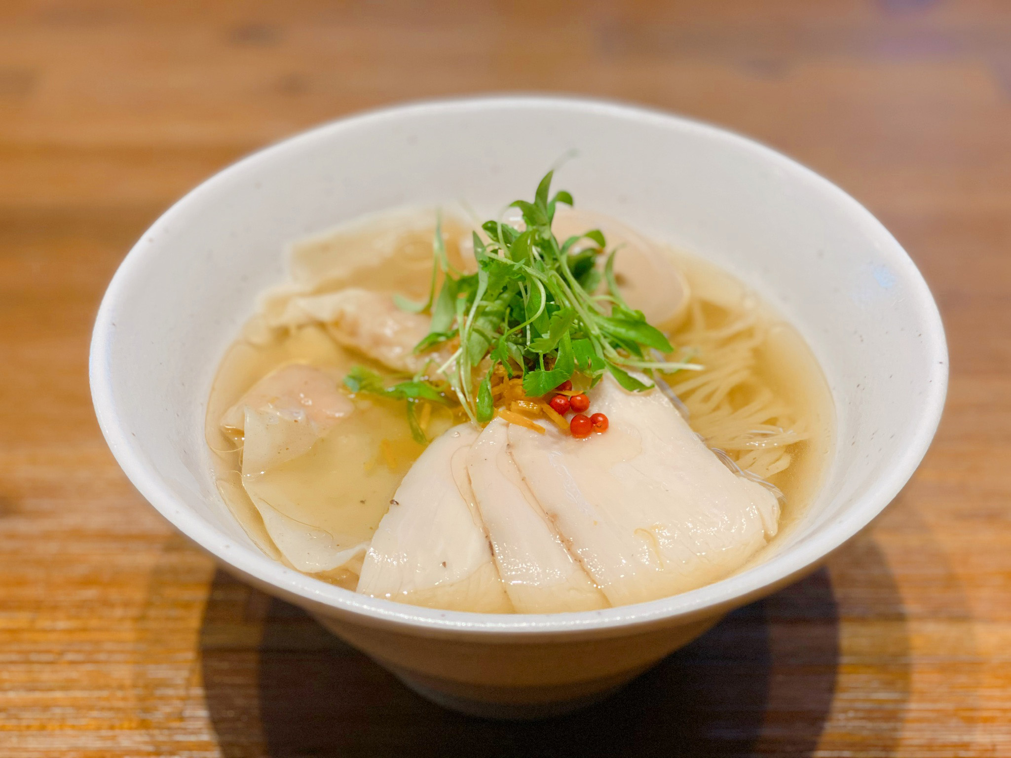 Yuzu shio ramen topped with thin slices of chicken in a white bowl.