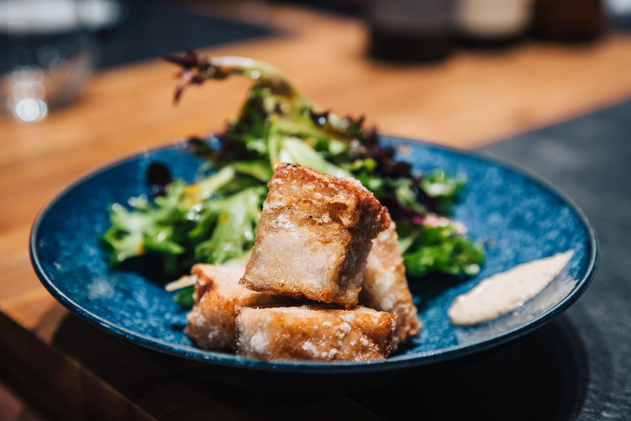 Cubes of deep-fried pork belly and salad greens on a blue plate.