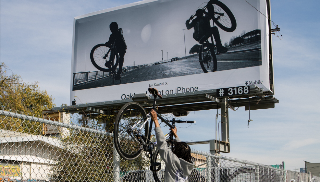 Omar "Meez" Jones lifting his bike toward a billboard which features his image.