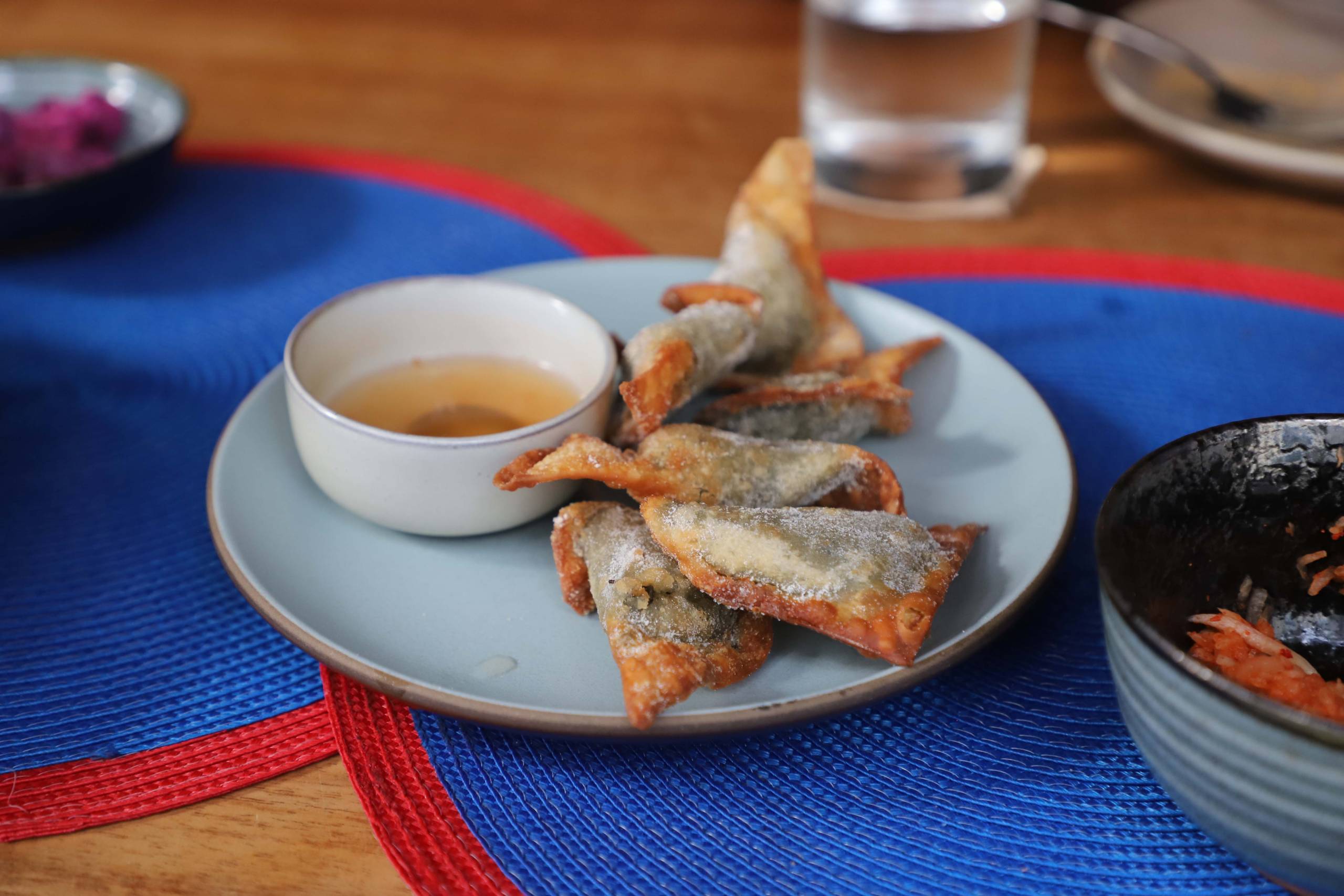 Crispy, triangular-shaped laing wontons on a plate with a side of dipping sauce. 