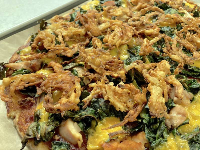 A biscuit crust pizza topped with crispy onions and collard greens.