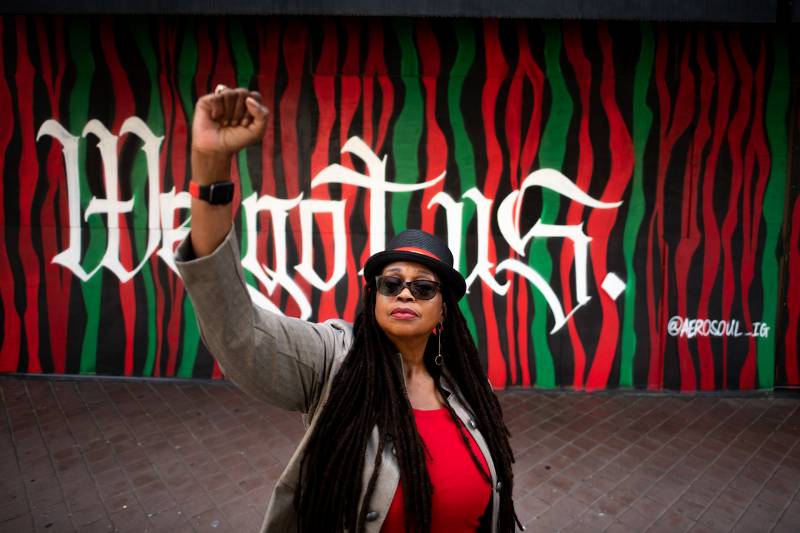 Ayodele Nzinga raises her fist in front of a mural that says, "We Got Us" by the organization AeroSoul in Oakland on July 19, 2021.