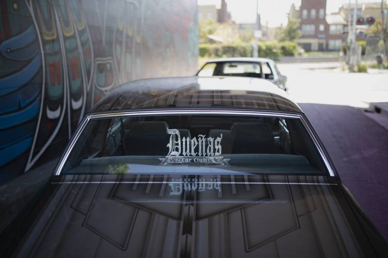 Looking at two low Riders, the Dueñas Car Club Logo is seen through a back window.