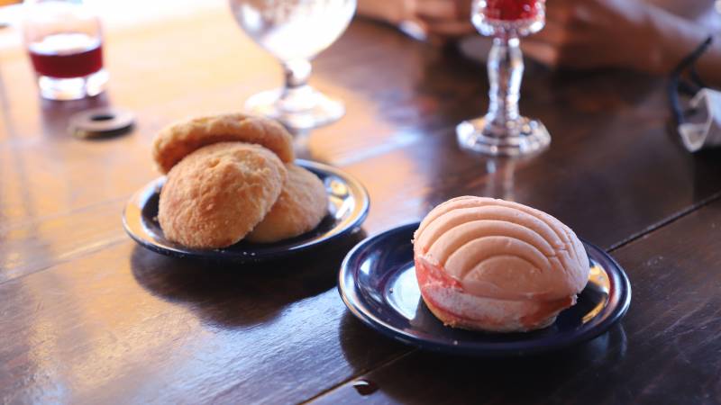 Conchas on a wooden table, with glasses of wine and hibiscus mimosa in the background.