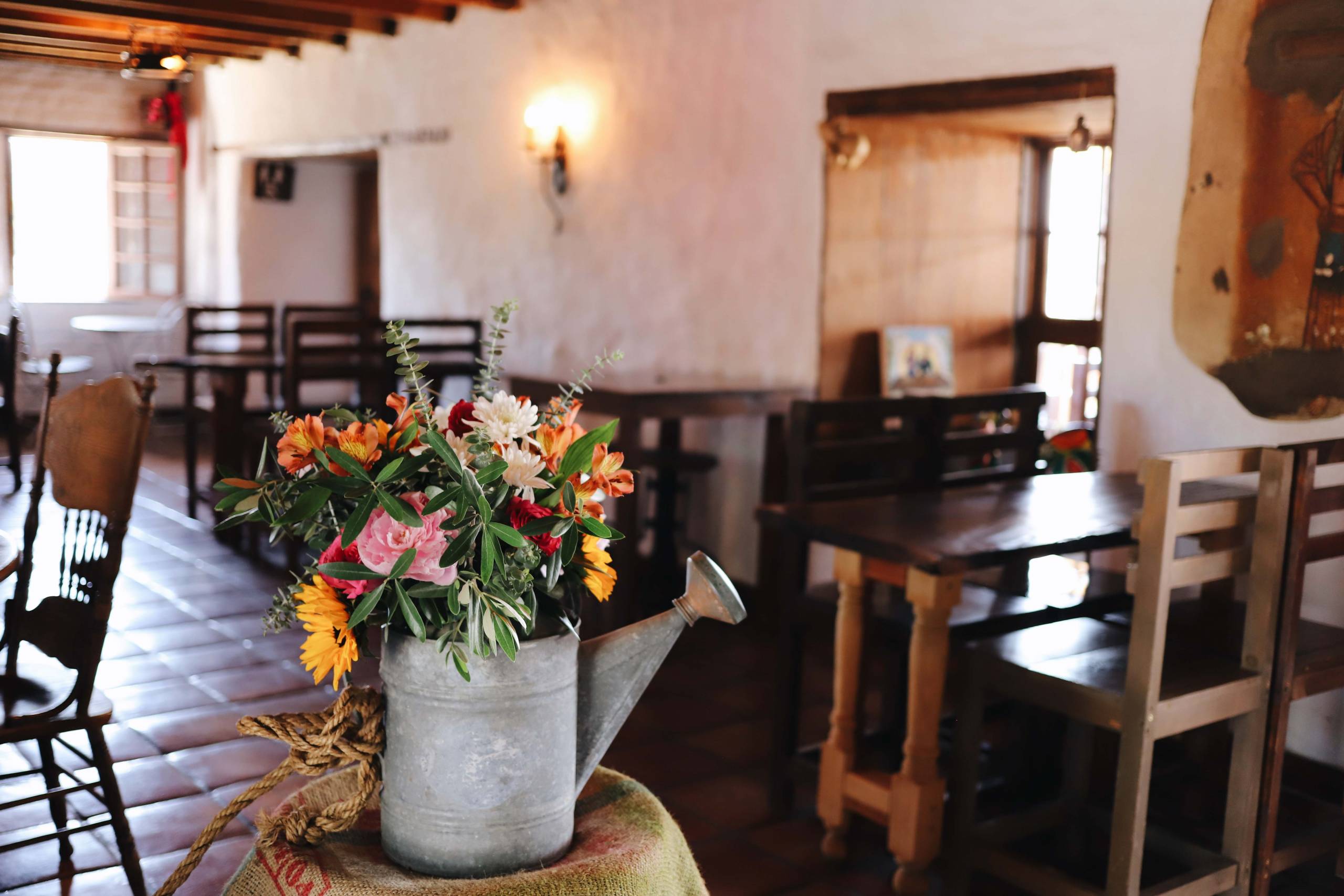 The dining room at La Cheve, with the old adobo walls and a bunch of flowers in a watering can.