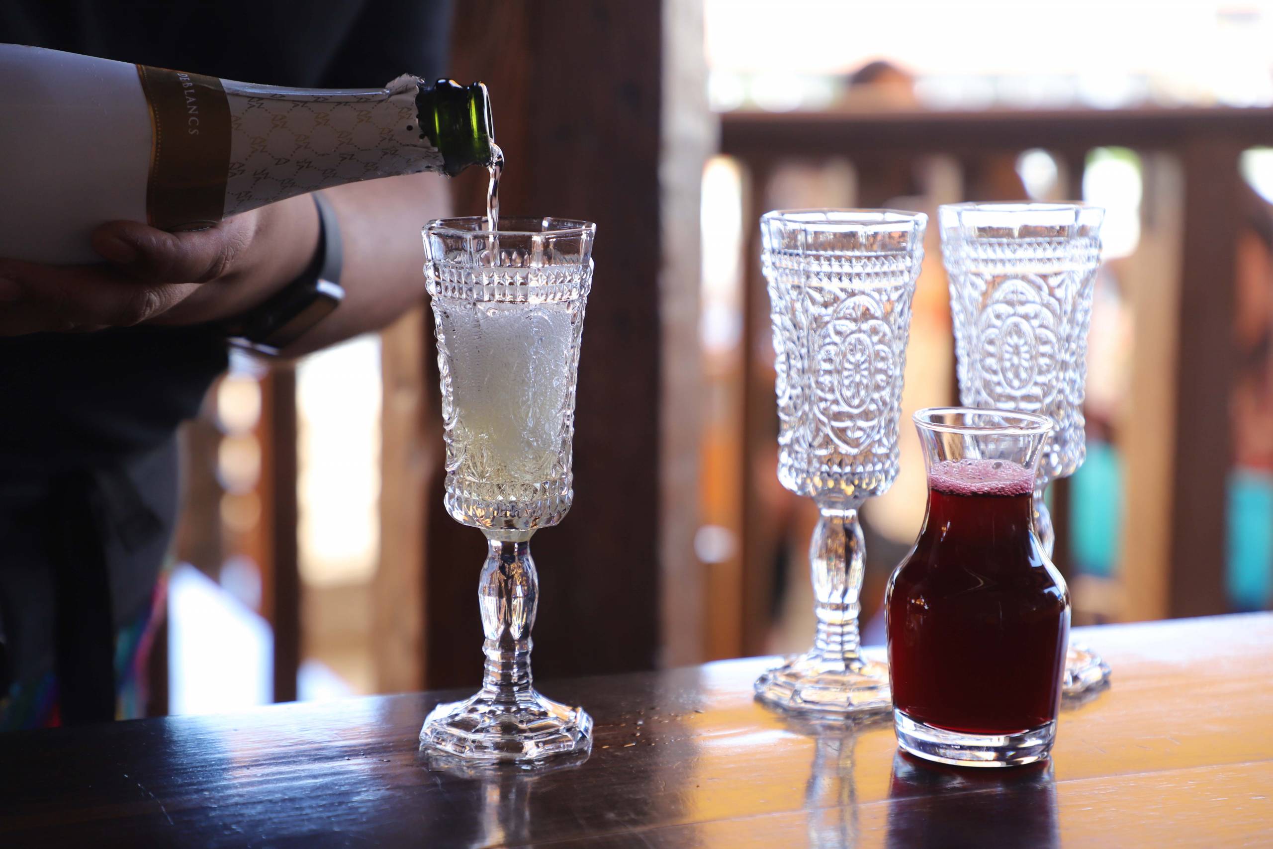 Wine being poured into a glass, with a small pitcher of hibiscus mimosa to the side.