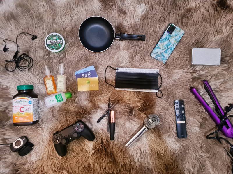 Items left to right, top to bottom: Headphones, vitamin C, webcam, mints, hand sanitizer, Playstation controller, pan, grocery cards, eye makeup implements, mask, karaoke microphone, phone, remote, speaker, hair straightener (purple).
