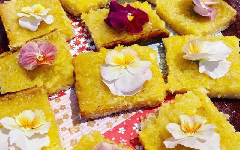 A spread of lemon bars topped with pink and red edible flowers.