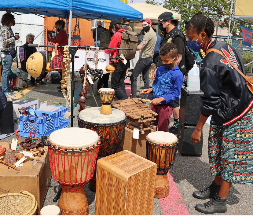 A young child tries playing African drums at an outdoor market.