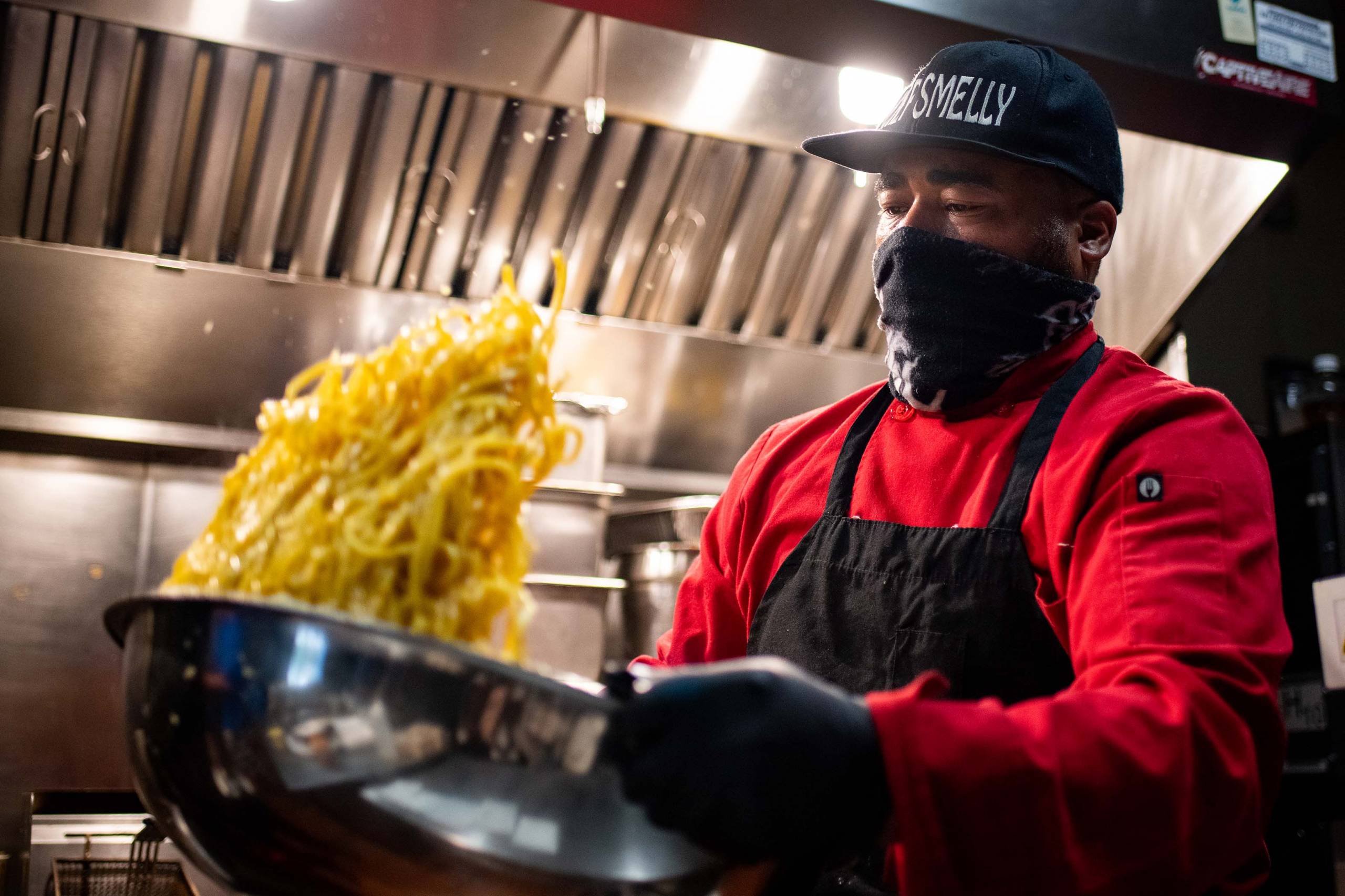 Chef Edward Wooley tosses a batch of garlic noodles in a large metal bowl. 