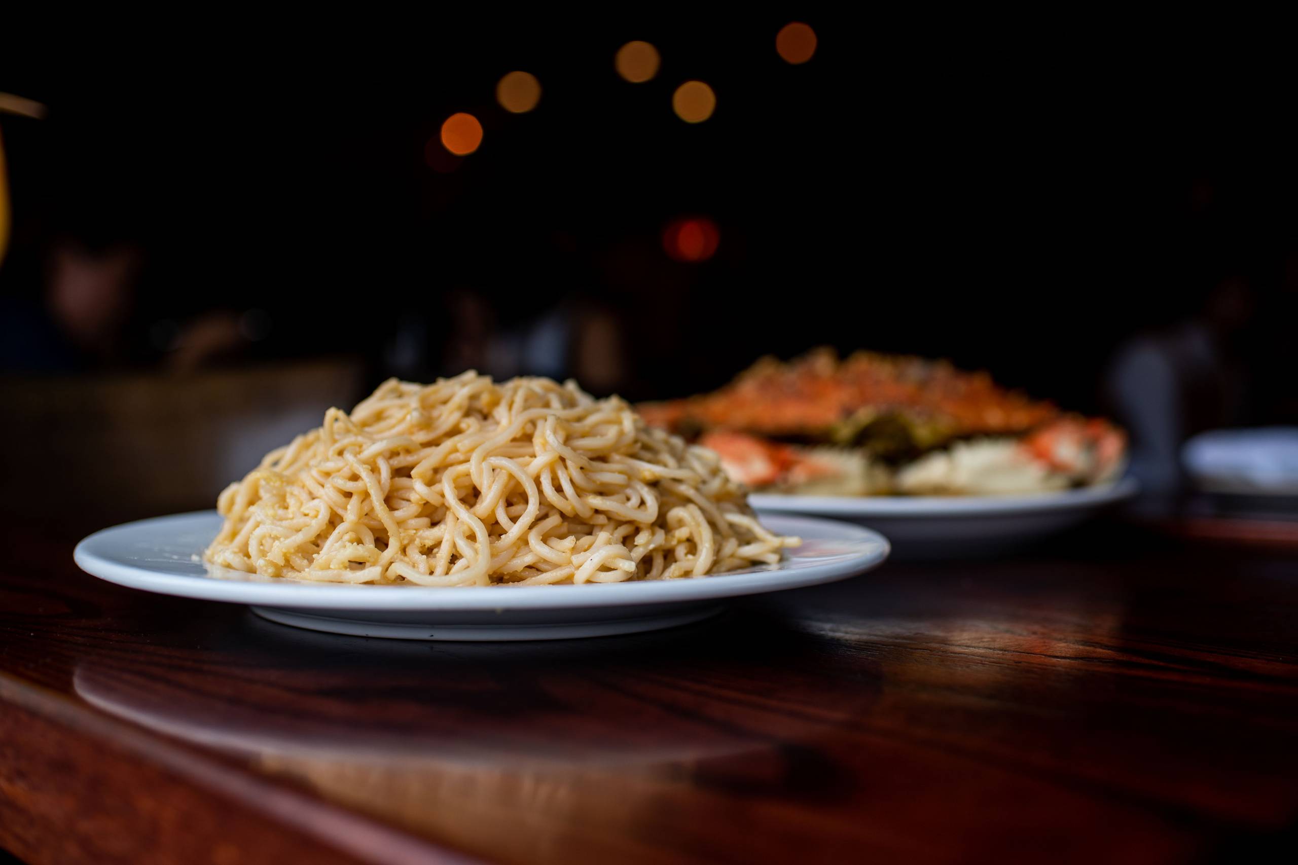 A plate piled high with garlic noodles on a table, in front of a plate of whole roast crab.