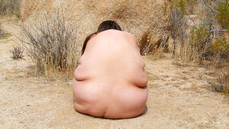 Woman's bare back in front of tan rock.