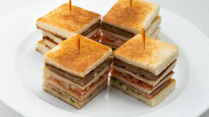 Four mini quadruple-decker sandwiches, each held together with a toothpick on top.