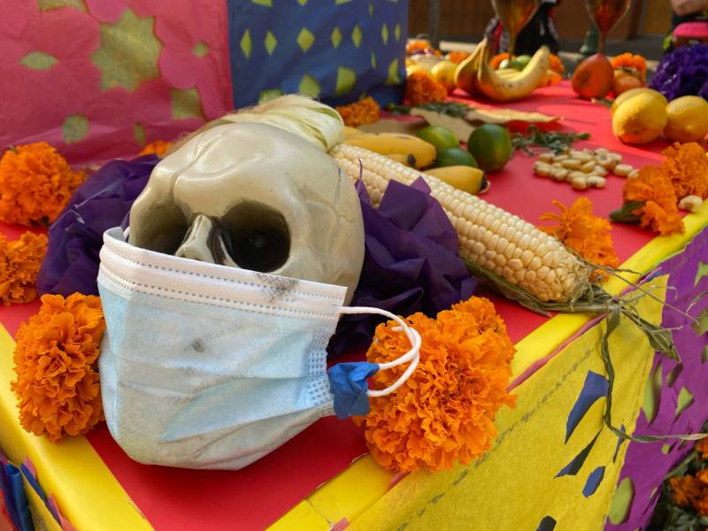 A Día de los Muertos family altar display featuring a skull wearing a face mask.