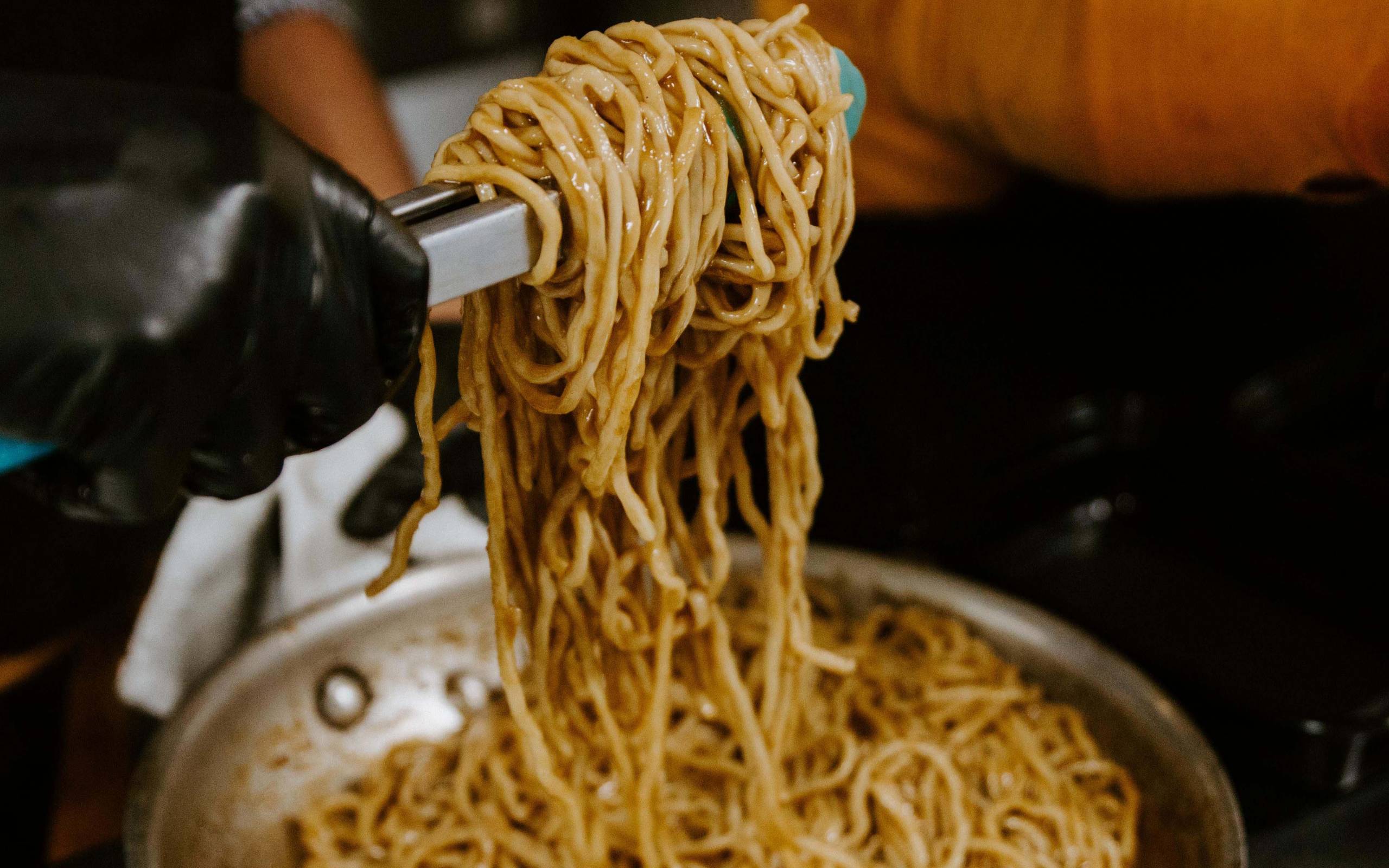 Saucy garlic noodles are mixed with a pair of tongs at Noodle Belly.