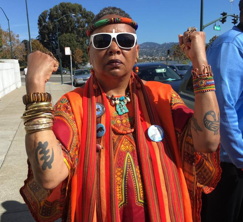 Charlotte Hill O'Neal wears sunglasses as she poses, showing her forearm tattoos and jewelry as she stands in front of the Alameda County Court House. 
