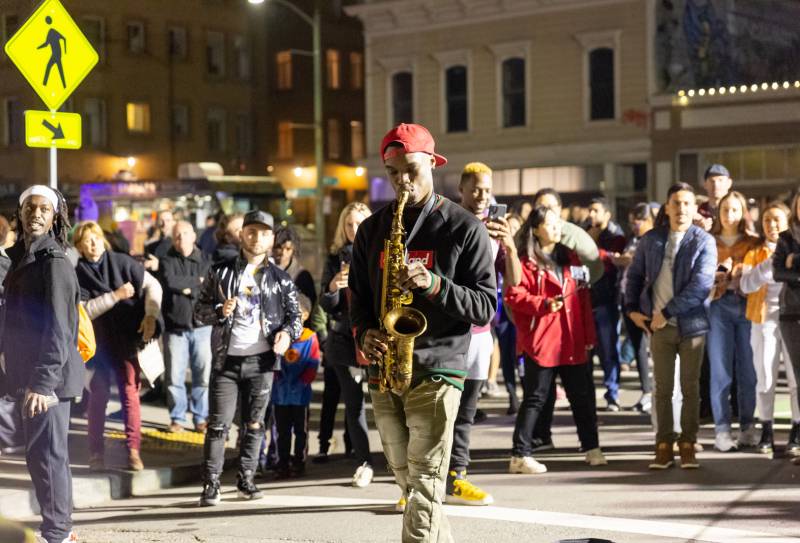 A saxophonist plays on the street at a street fair in Oakland.