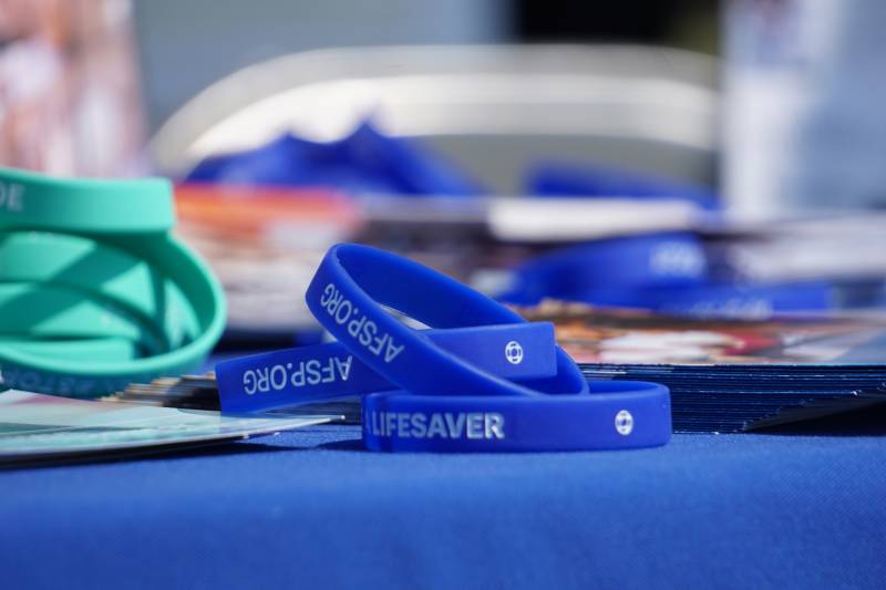 The word "Lifesaver" is inscribed on a wristband that sits on a table at a prior Out Of The Darkness event. 