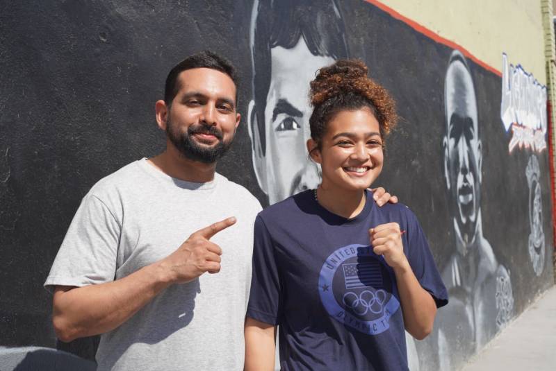 Outside of Lightning's Boxing Club in East Oakland Mario Bamberger and Daisy Bamberger pose for a photo in front of a mural of boxing legends. 