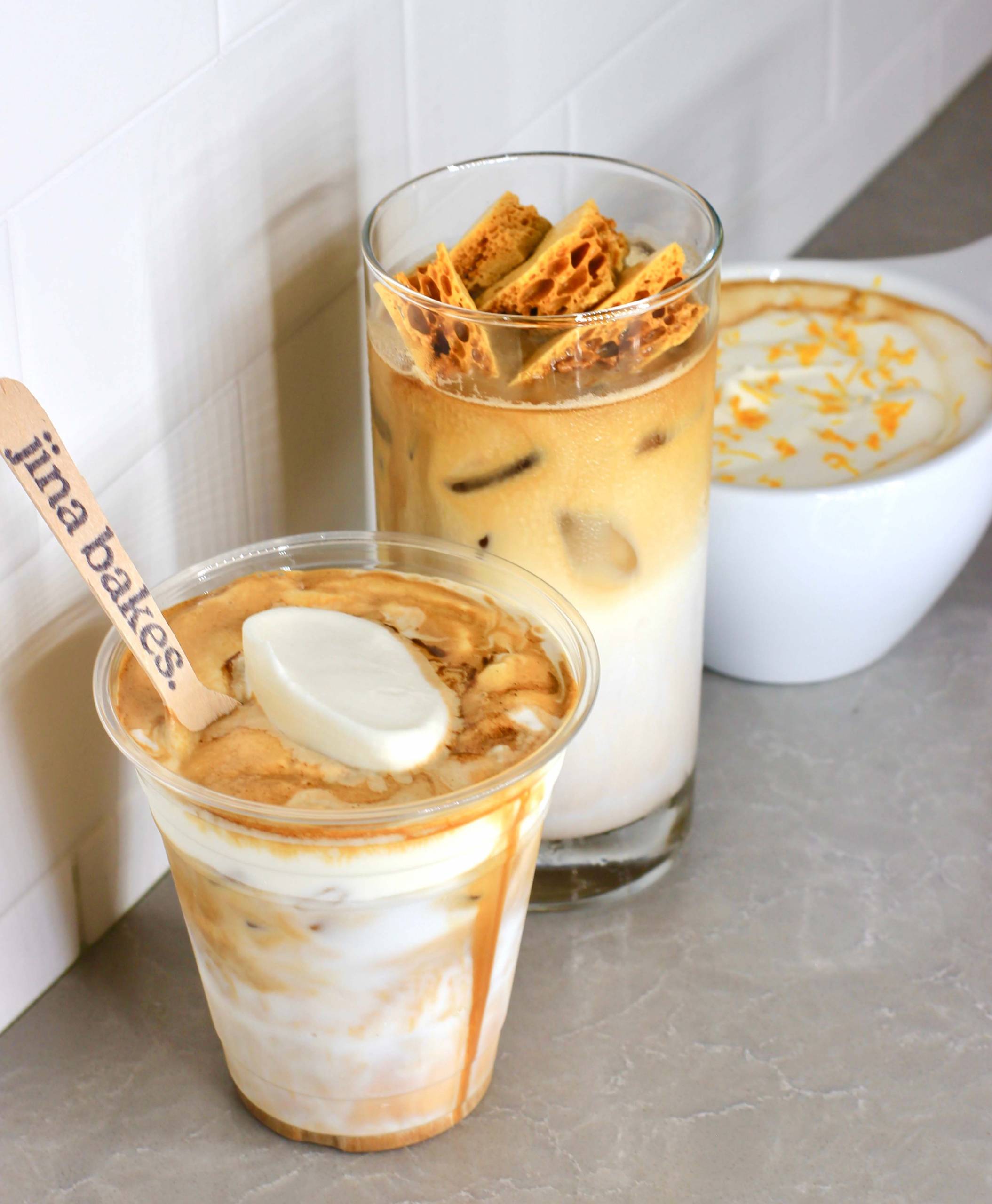 Three coffee drinks on a countertop, variously topped with whipped cream and honeycomb toffee candy.