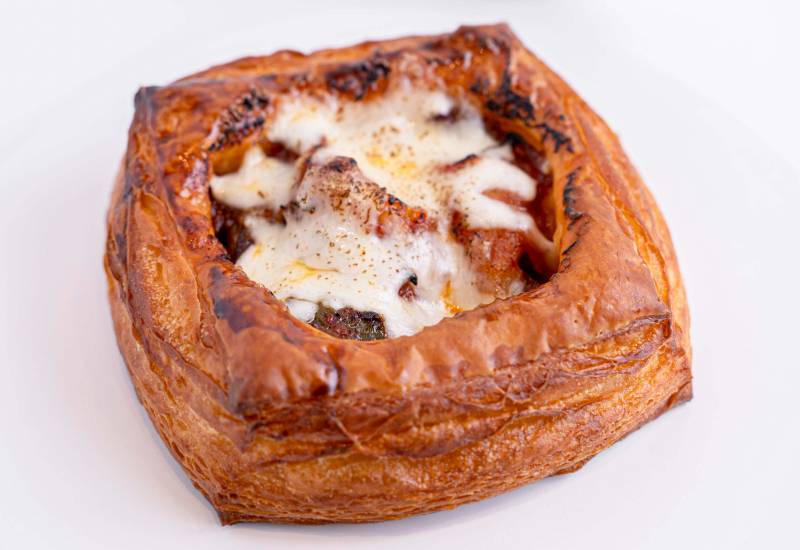 A square croissant topped with meat and charred, melted cheese.