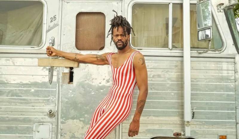 A man in a red-and-white striped unitard leaning against a RV.