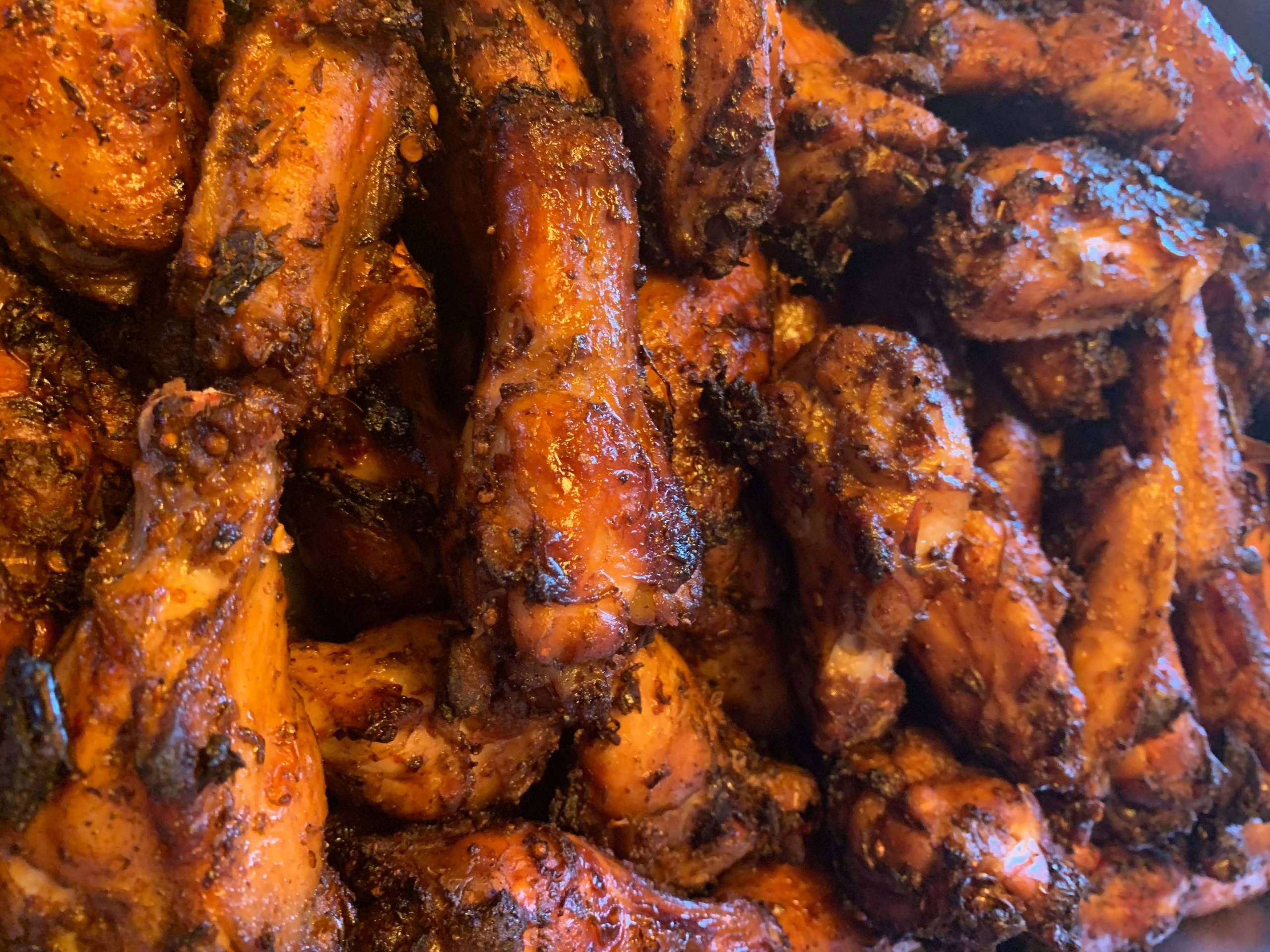 Close-up of a tray of red, spice-stained chicken wings with a hint of charring.
