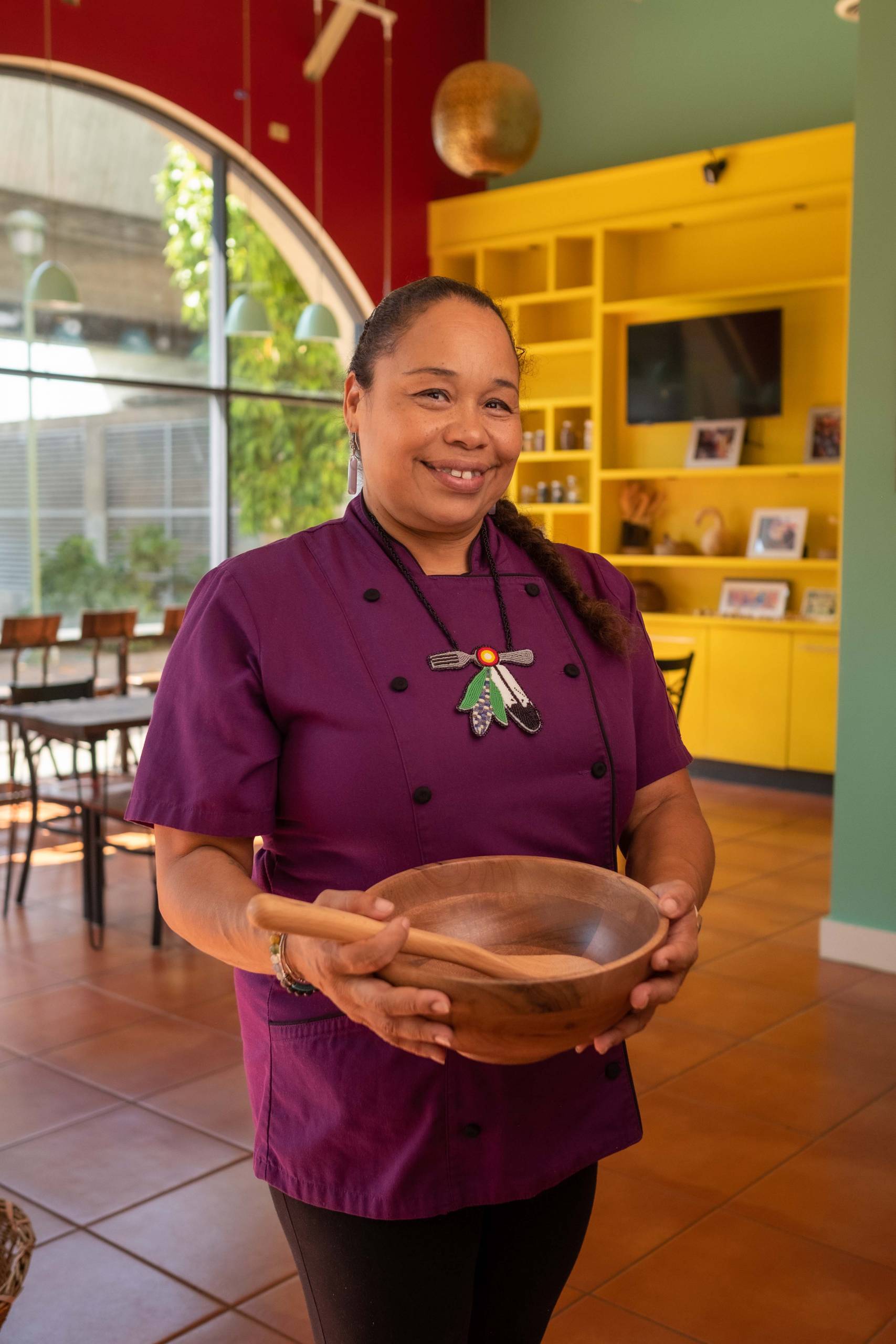 A chef holds a wooden bowl inside her restaurant.