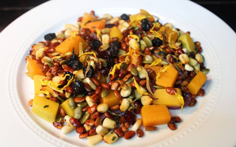 A colorful salad featuring corn, beans and squash on a white plate.