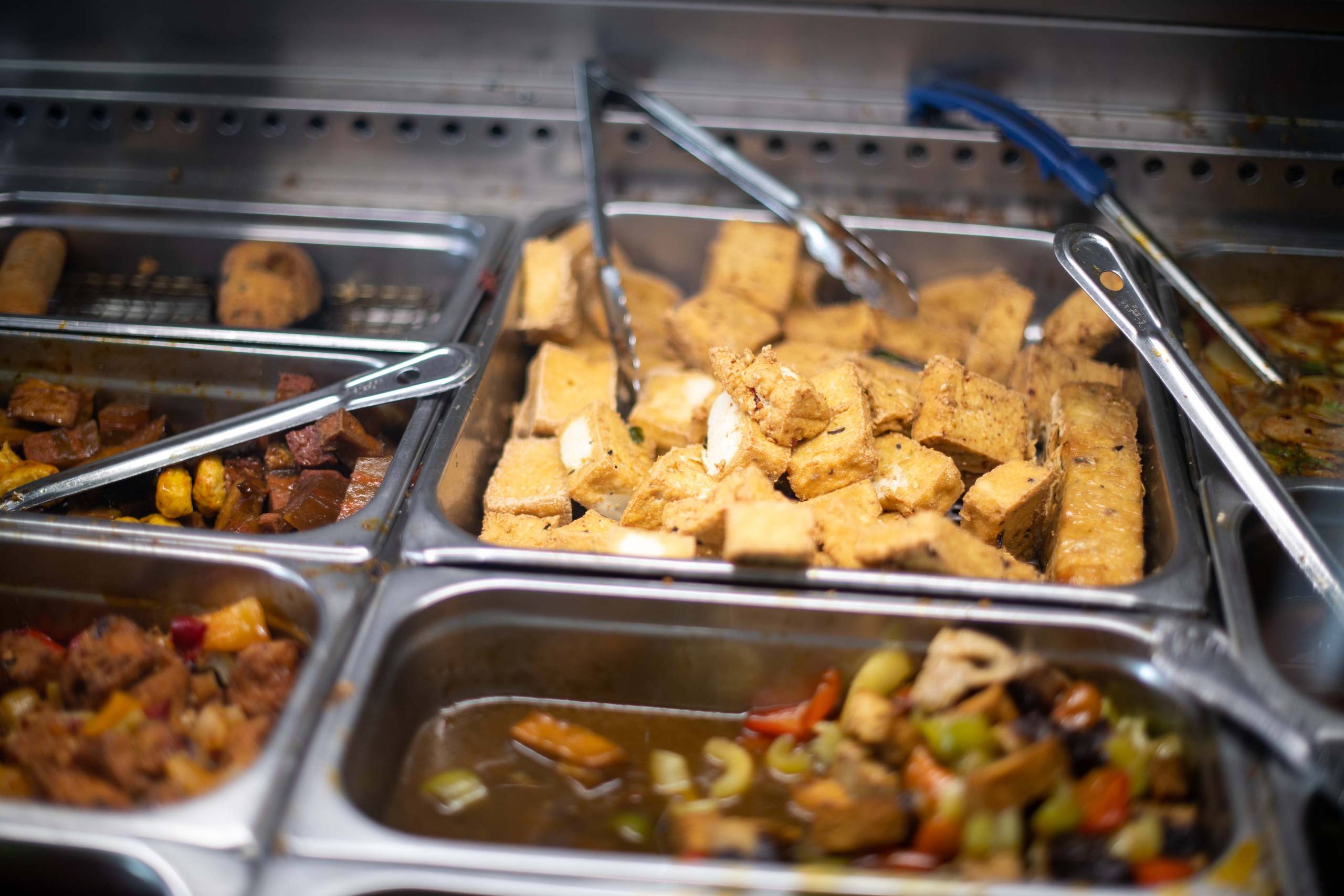 A steamer tray full of freshly fried tofu, as part of a buffet-style display.