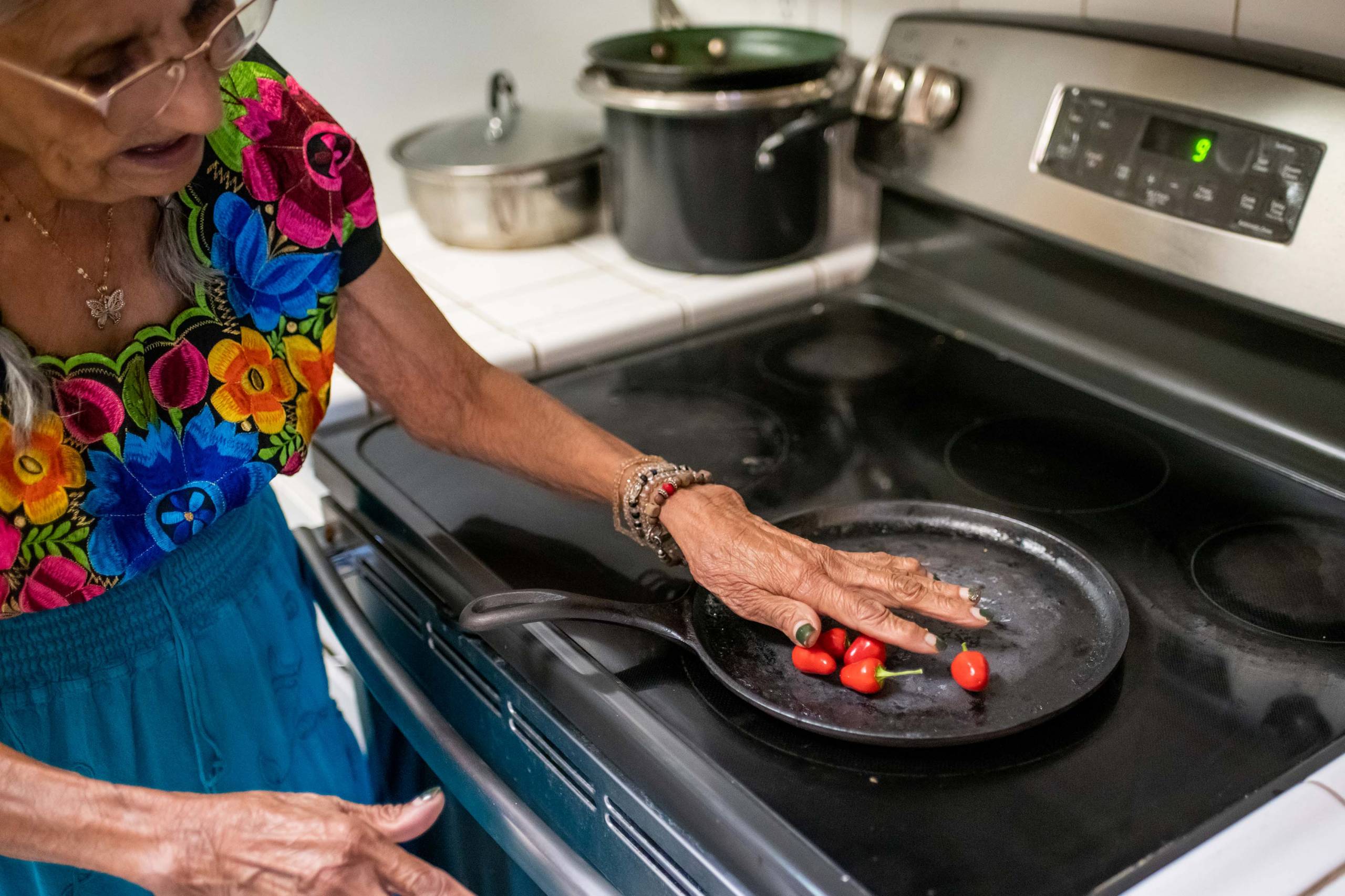 A woman toasts chile peppers in a cast iron pan.