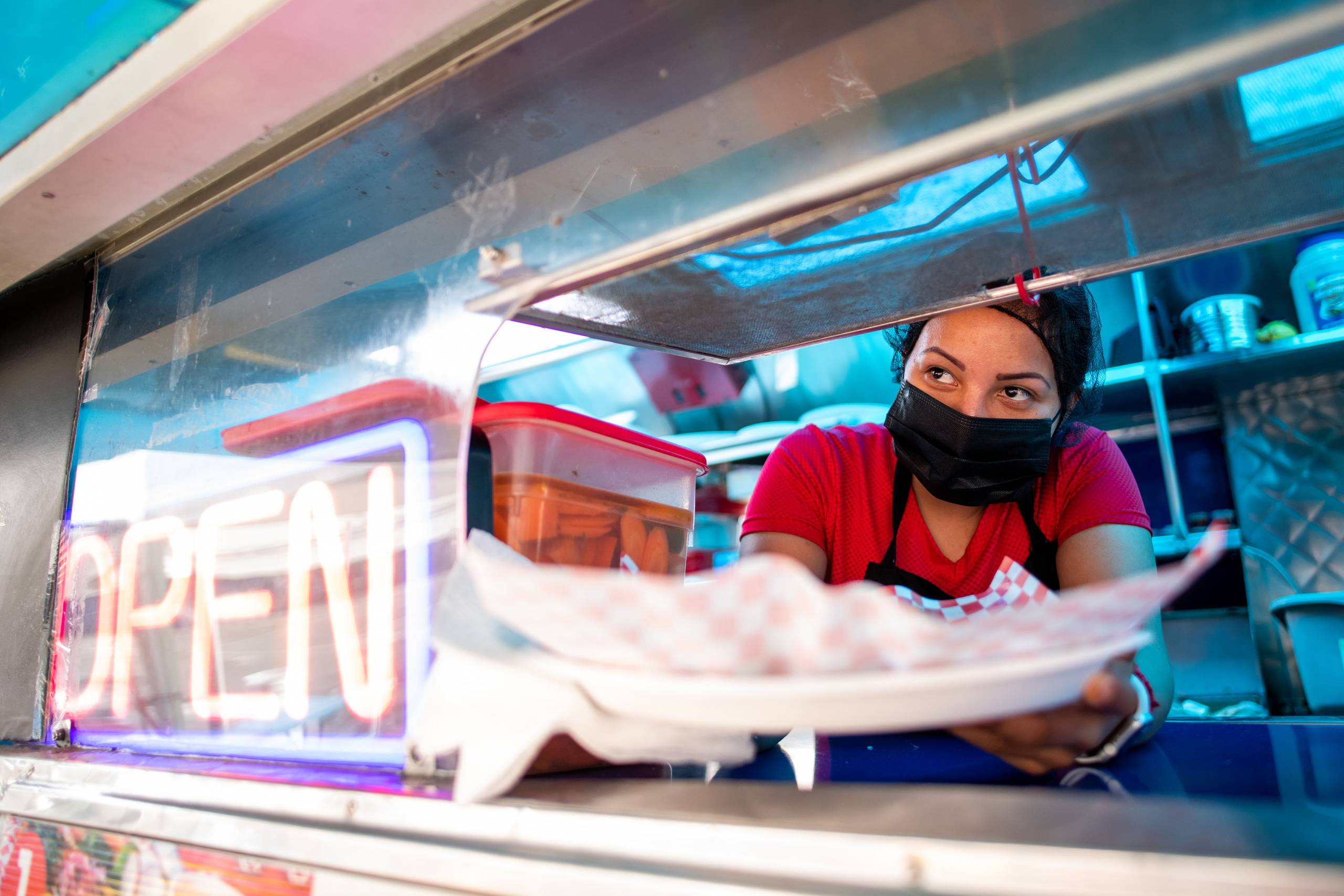 A taco truck employee hands a plate of food to a customer through the window.