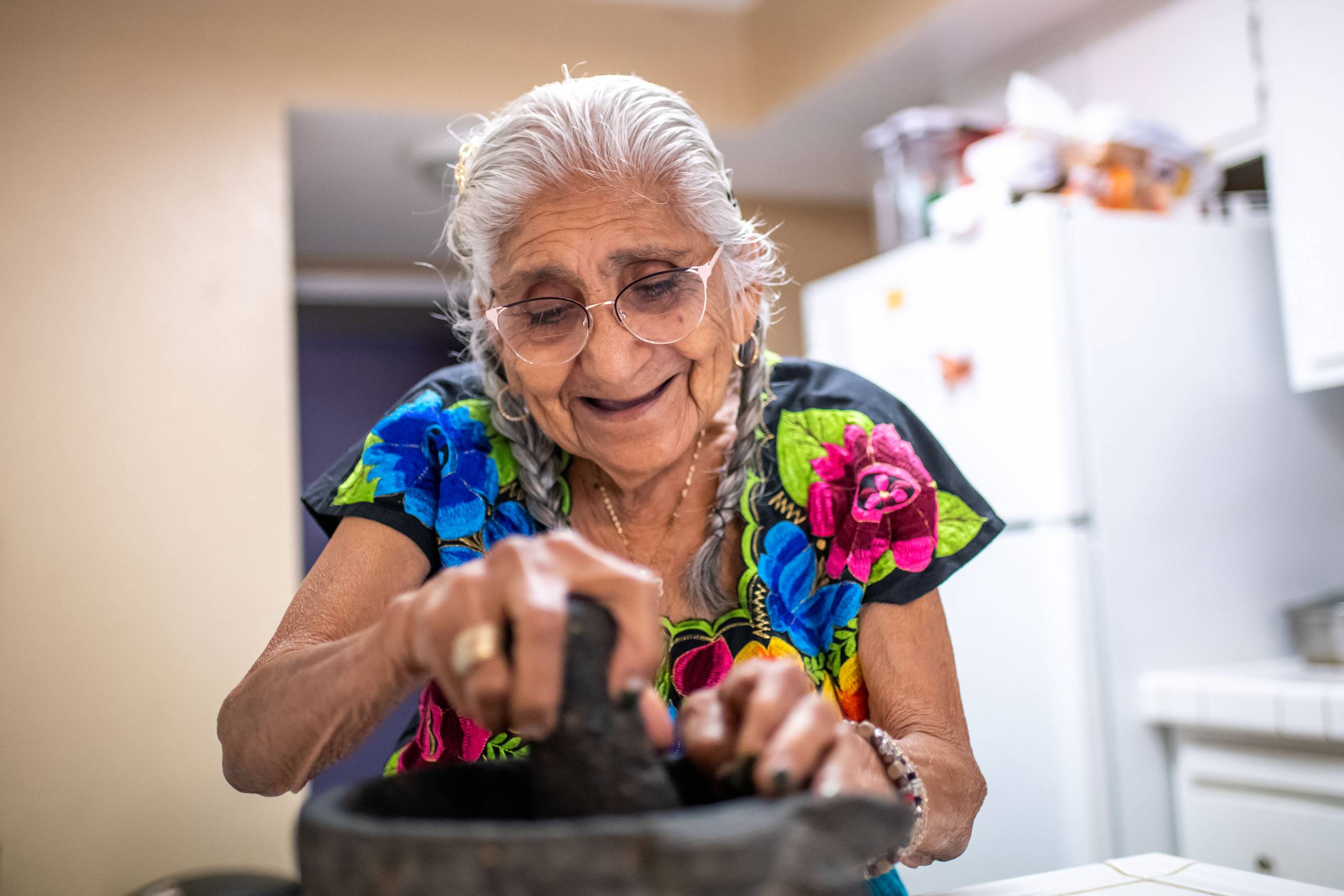 An elderly Latina woman grinds ingredients inside a stone molcajete.