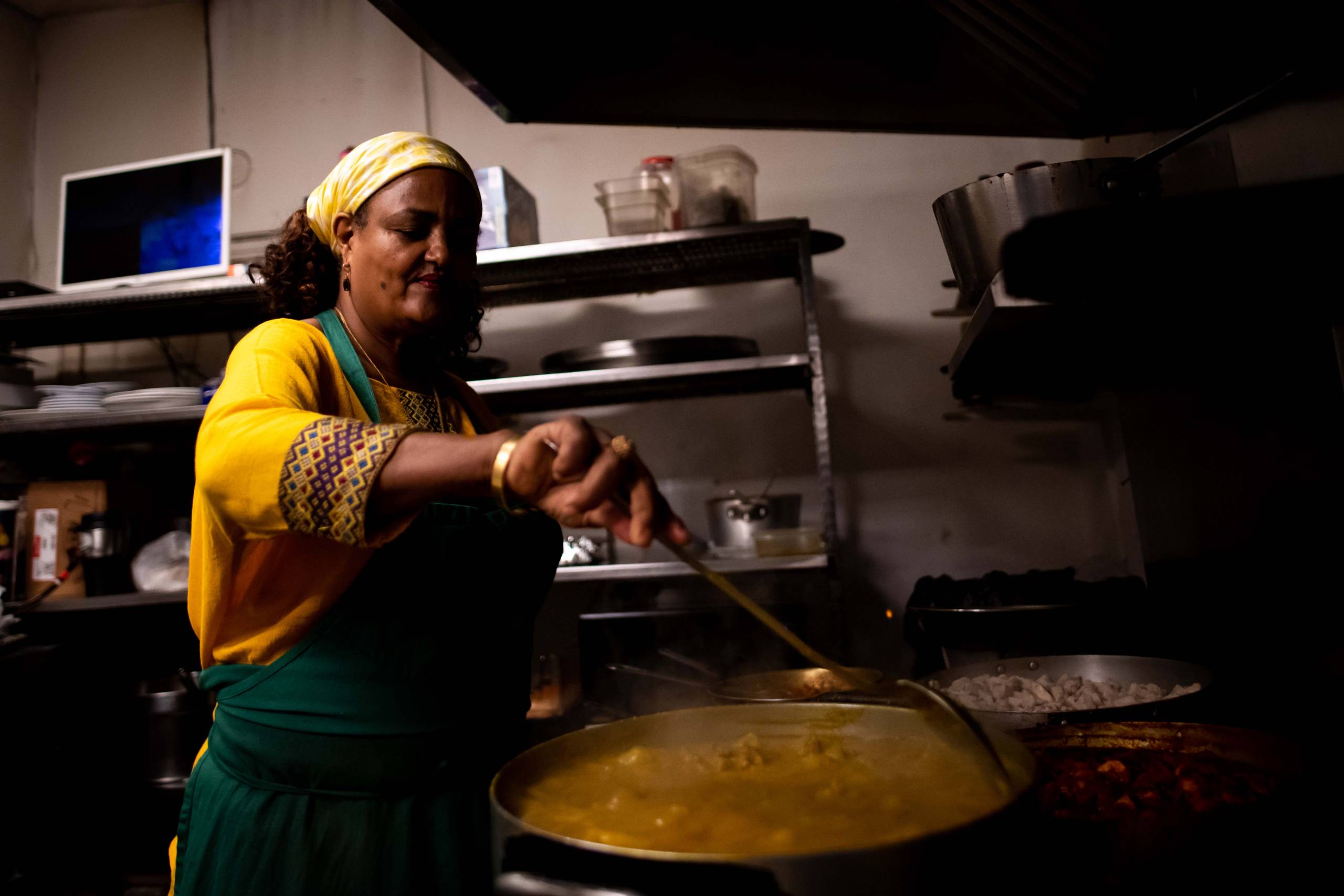 A woman cooks a large pot of stew in a restaurant kitchen.