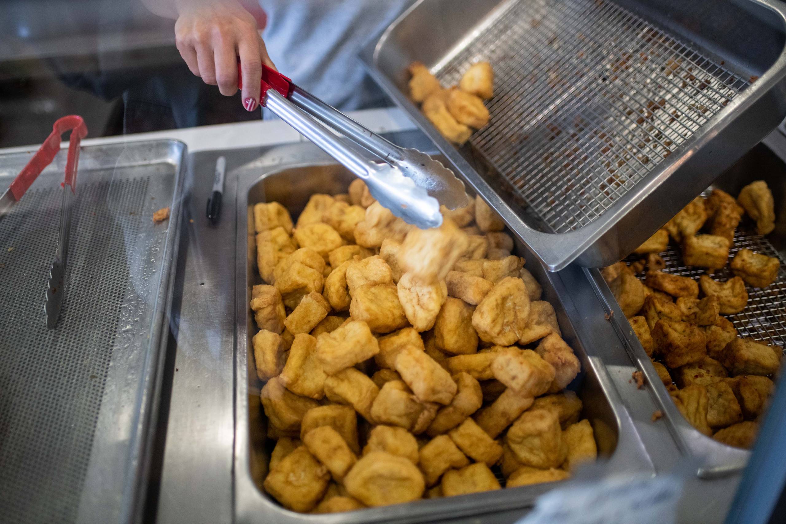 An employee refills a metal display case with freshly fried tofu.