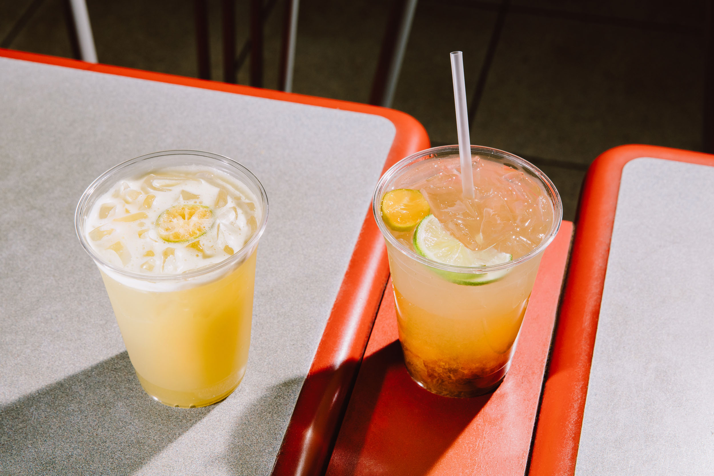 Two cups of iced sugarcane juice on a mall food court tabletop.