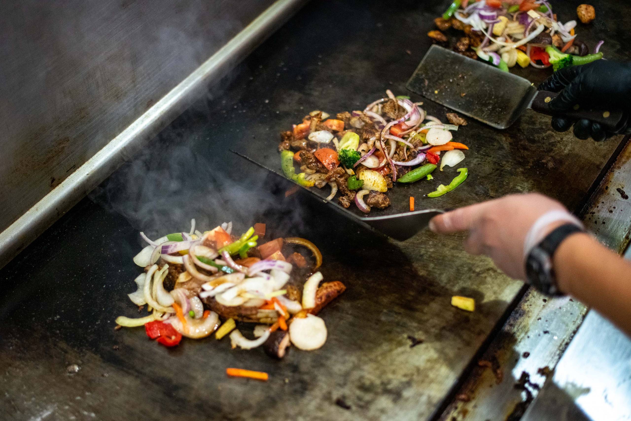 Meat and vegetables sizzling on a hot flat-top grill.