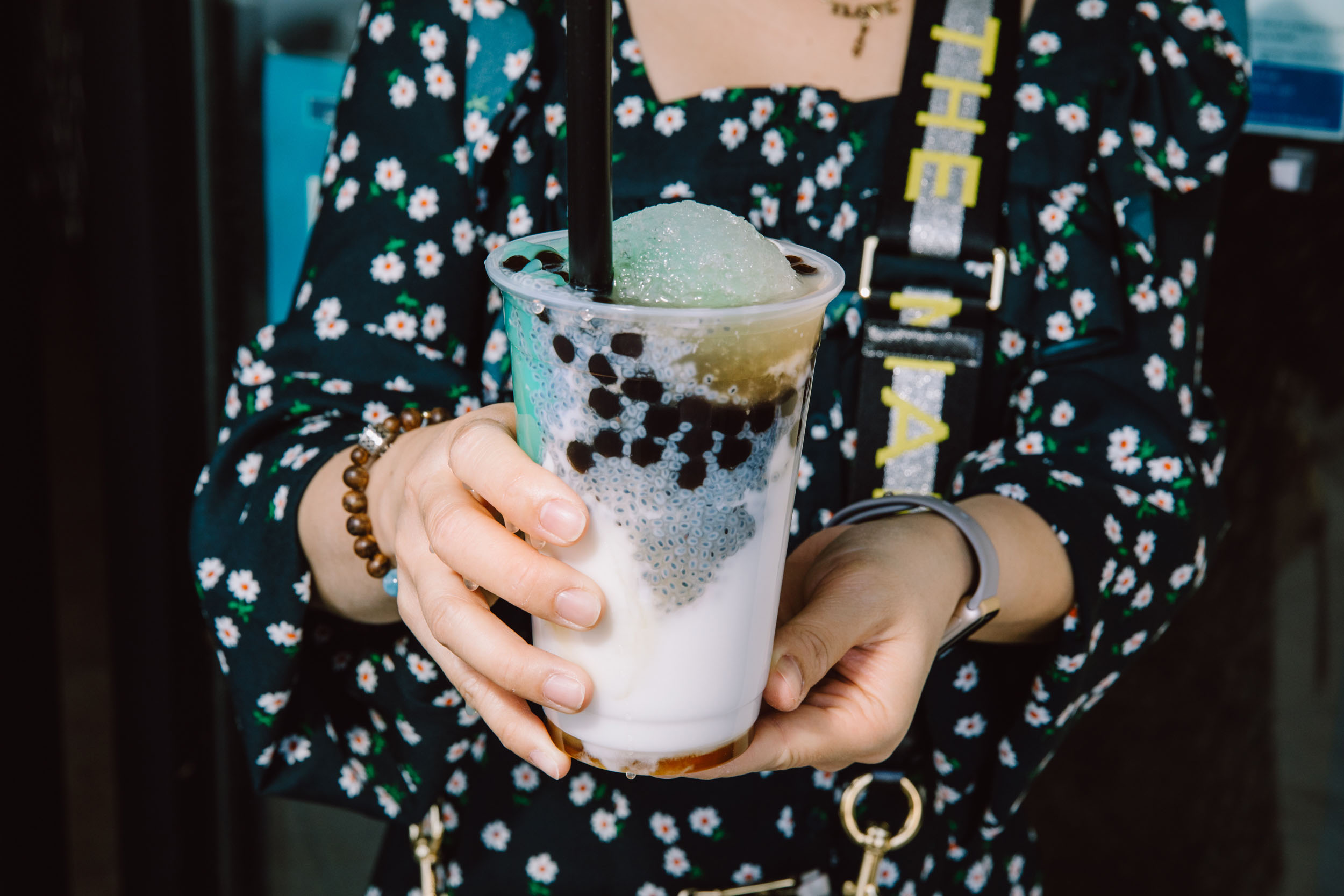 A woman holds a soy pudding drink dotted with boba, pandan and shaved ice.