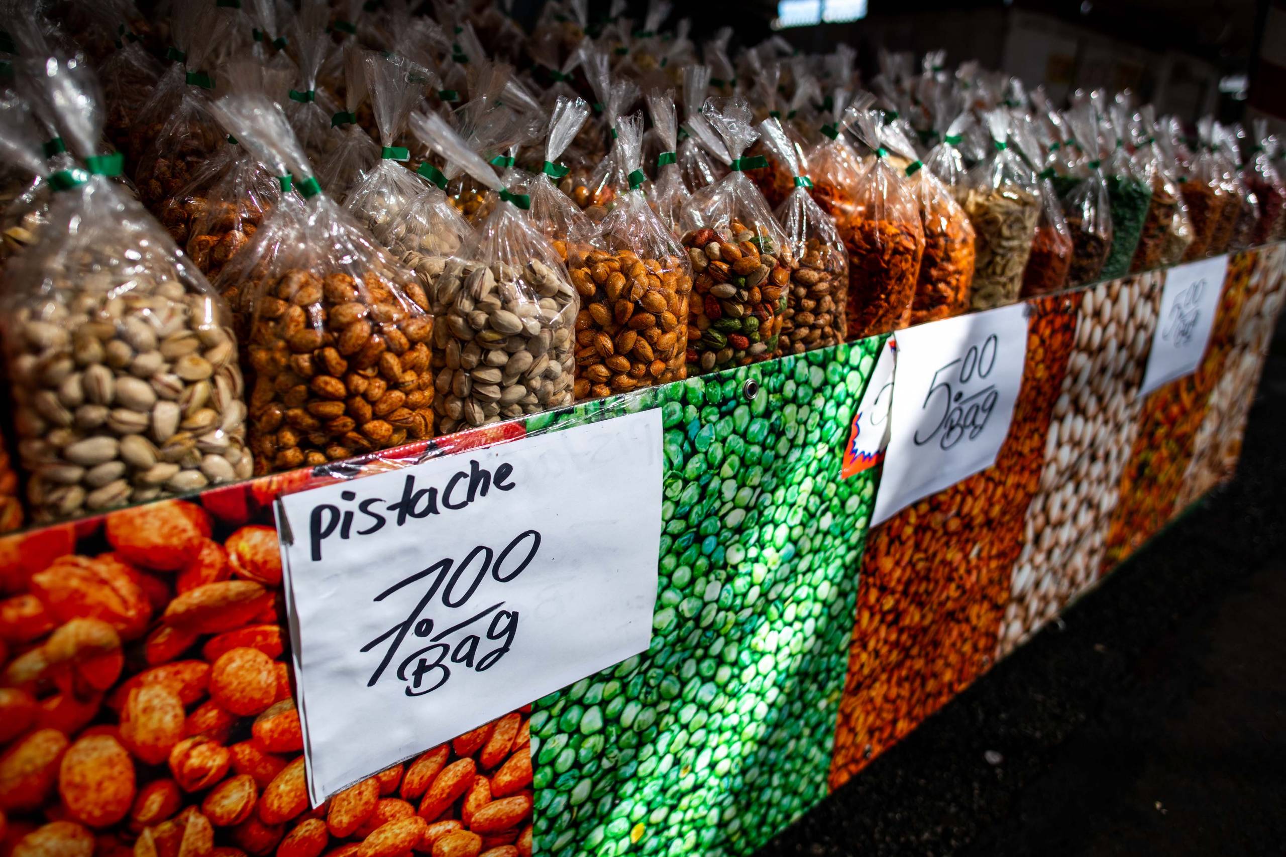 Bags of flavored pistachios of all different colors, displayed at an outdoor market stand.