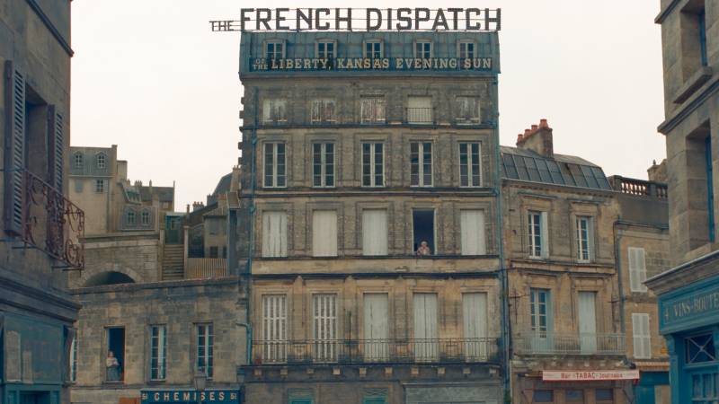 A light brown building with five floors, each featuring five identical windows. A sign reading 'The French Dispatch' sits atop the building.