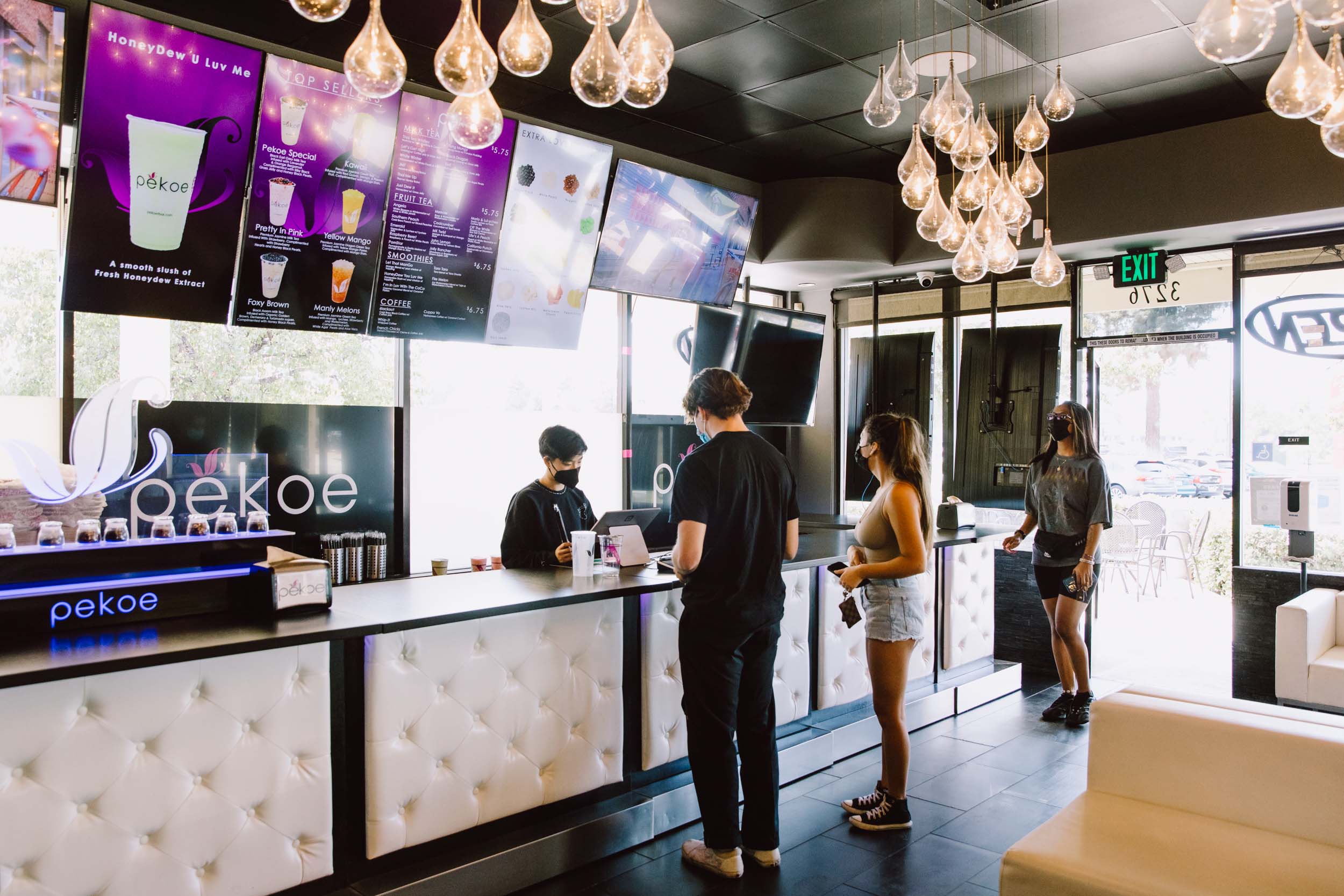 Young Asian Americans stand in line to order boba inside a shop with ornate light fixtures.